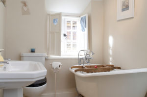 The Honeypot Cottages bathroom with delightful, traditional bathroom complete with wood bath shelf and shutter window covers.